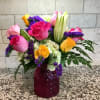 Mixed bouquet of pink and yellow roses, lilies and white blooms in a red glass vase on a speckled counter.