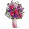 Pink roses, purple blooms, and white daisies in a pink ombré vase with a metal butterfly accent