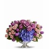 Low centerpiece of purple roses, pink spray roses, tulips, and blue hydrangeas in a silver pedestal bowl