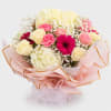 Bouquet of pink and cream roses, carnations, and hydrangeas wrapped in pale pink paper