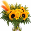 Yellow roses and sunflowers in a clear glass vase with orange and yellow feathers