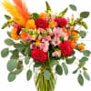 Bright mixed bouquet of red, pink, orange, and yellow flowers in a glass vase