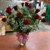 Red roses in a clear glass vase with a pink ribbon