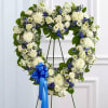 Heart-shaped floral wreath with white and blue flowers on a stand