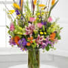 Tall mixed bouquet in a clear glass vase with pink, purple, orange, and yellow flowers