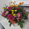 Mixed bouquet of pink roses, yellow mums, and orange flowers in a white basket