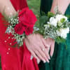 Two floral wrist corsages, one red and one white, worn on hands