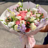 Hand-tied bouquet of pink, white, and lavender flowers wrapped in pale pink paper