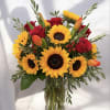 Bouquet of sunflowers, red roses, and orange tulips in a glass vase