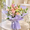Pastel bouquet of roses, calla lilies, and mixed blooms wrapped in lavender paper
