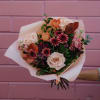 Bouquet of blush roses, pink blooms, and dark purple flowers wrapped in pale paper