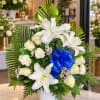 White lilies and roses arranged in a vase with a blue ribbon bow