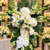 White floral cross arrangement with lilies, roses, and a ribbon bow