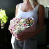 Woman holding a pink heart-shaped box of pastel flowers and macarons