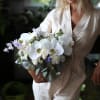 Woman holding a white and lavender bouquet with orchids and roses