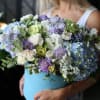Woman holding a large bouquet of blue, purple, and white flowers in a blue box