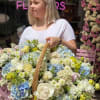 Woman holding a large basket of pastel flowers outside a flower shop
