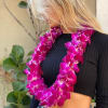 Woman wearing a bright pink orchid lei over a black top