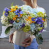 Large bouquet of blue, yellow, and white flowers in a wrapped container