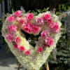 Heart-shaped floral arrangement with pink roses and white flowers on an easel