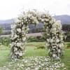 White floral arch outdoors with petals scattered on grass