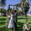 Bride and groom standing under a floral wedding arch by the beach