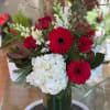 Red gerbera daisies and roses with white hydrangea in a glass vase