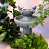 Stone birdbath fountain surrounded by potted houseplants