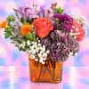 Mixed bouquet of orange, purple, and pink flowers in an amber glass vase