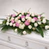Pink and white rose casket spray with greenery on a white coffin