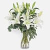 White lilies in a clear glass vase with eucalyptus foliage
