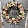 Standing wreath of pink daisies, white roses, and lilies on a green easel.