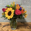Bright mixed bouquet with sunflowers, lilies, carnations and other blooms in a clear glass vase