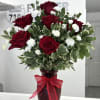 Arrangement of red roses and small white flowers in a red glass vase with a bow.