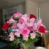 Pink lilies and roses arranged in a clear glass vase with a pink ribbon.
