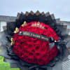Large bouquet of red roses wrapped in black paper with a crown and ribbon