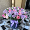 Lavender and pink roses arranged in a round box with a ribbon