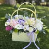 Basket of pastel flowers with a lavender ribbon on grass