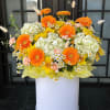 Bright mixed flower arrangement in a white box with orange and yellow blooms