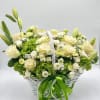 White basket arrangement of cream roses, lilies, and green hydrangeas with a green ribbon