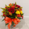 Mixed bouquet of red, orange, and yellow flowers in a glass vase with an orange ribbon