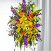 Tall floral standing spray with yellow lilies, orange roses, and purple flowers