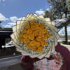 Bouquet of yellow roses with white filler flowers wrapped in layered paper
