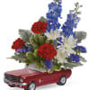 Floral arrangement in a red toy car container with red, white, and blue flowers