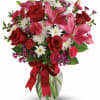 Bouquet of red roses, pink lilies, and white daisies in a glass vase with a red ribbon