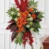 Tall standing spray of red gladiolus, orange lilies, and green carnations on an easel beside a casket.