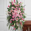 Tall standing spray of pink roses, lilies, and carnations on an easel beside a casket