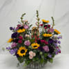 Colorful mixed flower arrangement with a small religious figurine in a rustic container