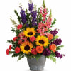 Mixed bouquet with sunflowers, roses, carnations, and purple spikes in a gray vase
