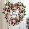Heart-shaped floral wreath with pink roses and white blooms on a stand